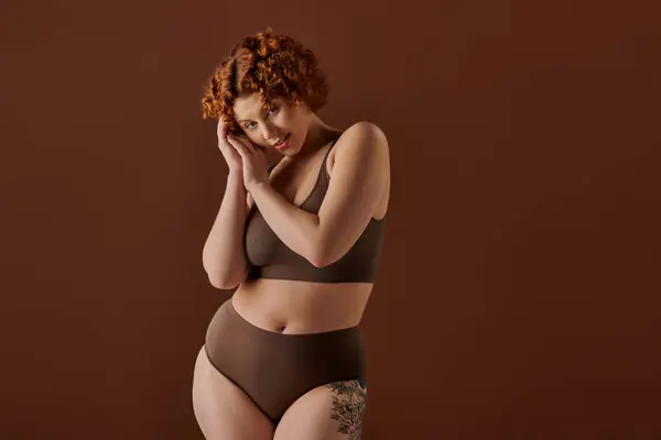 Young, curvy redhead woman exudes confidence in brown bikini on brown background. — Stock Photo