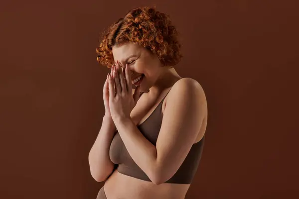 Curvy redhead woman in brown bikini, hands covering face delicately. — Stockfoto
