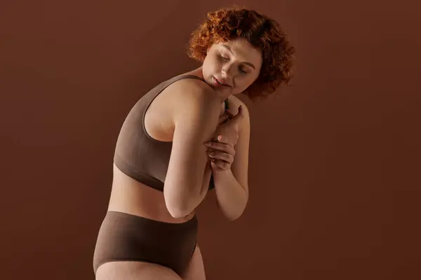 A young, curvy redhead woman confidently poses in a brown bikini for a captivating shot. — стокове фото
