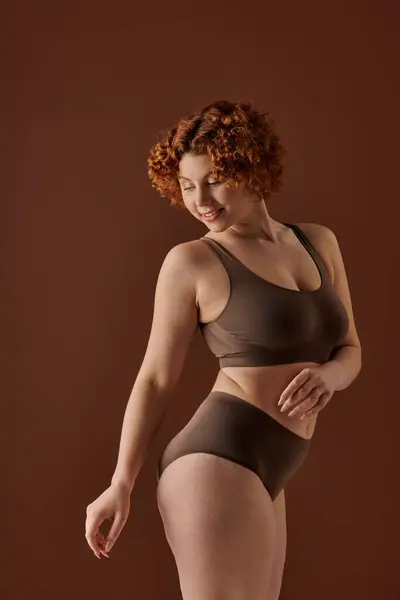 A curvaceous redhead woman is confidently posing in a brown bikini. — Stock Photo