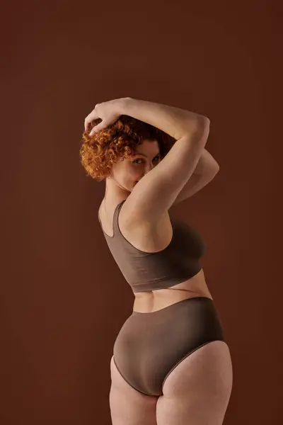 Young, curvy redhead woman in brown bikini striking a pose confidently. — стоковое фото