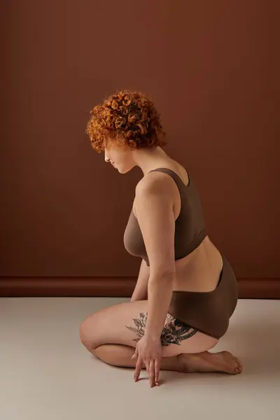 Young, curvy redhead woman in brown bikini crouching gracefully on the floor. — Stock Photo
