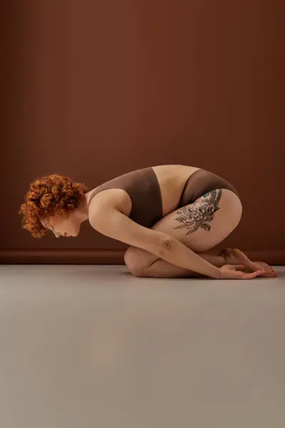 A curvy redhead crouches on the floor displaying her vibrant tattoos. — Stock Photo