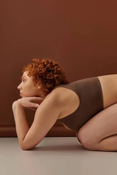 Curvy redhead woman in bikini crouching on floor — стокове фото