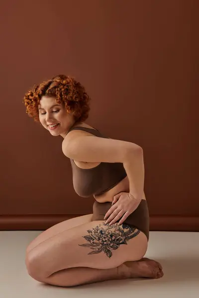 Curvy redhead woman sitting on floor with thigh tattoo. — Stock Photo
