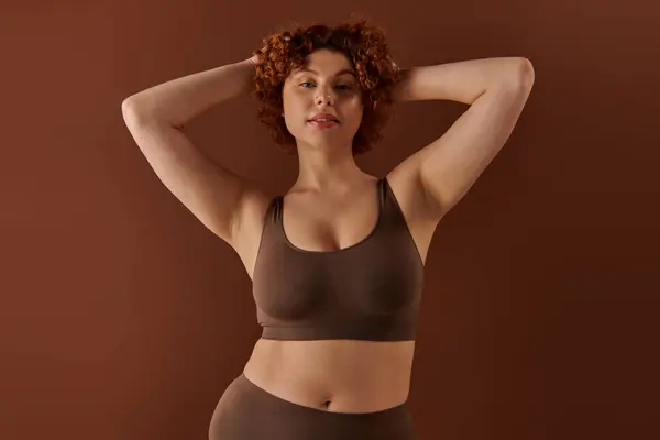 Young curvy woman exudes confidence in a brown sports bra on a brown background. — Stock Photo