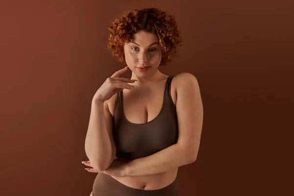 Young curvy redhead woman exuding confidence in brown bra on soft brown backdrop. — Stock Photo
