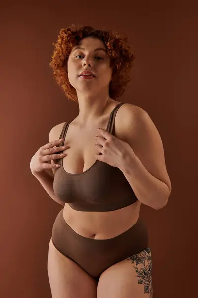 Curvy redhead woman in a brown bikini striking a pose on a matching brown background. — стокове фото