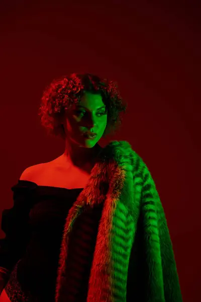 A young curvy redhead woman in a fur coat striking a pose in front of a vibrant red light. — Stock Photo