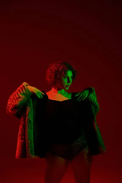 A young, curvy redhead woman strikes a pose in front of a vibrant red light. — Stock Photo