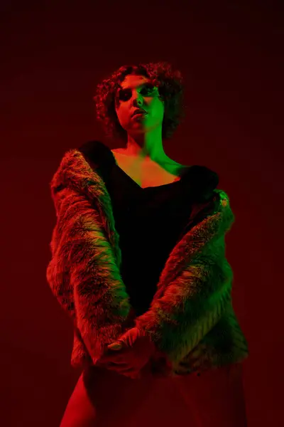 Curvy redhead in fur coat striking a pose under a bold red light. — Stockfoto