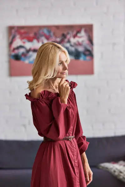 Eine reife Frau in einem auffallend roten Kleid steht anmutig in einem gemütlichen Wohnzimmer. — Stockfoto