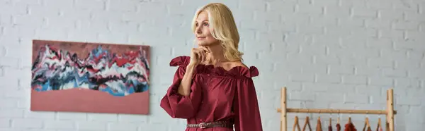 Una mujer madura en un vestido rojo se levanta con gracia en una habitación de lujo. - foto de stock