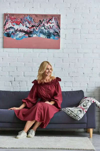 Stylish woman in red dress sitting on a couch. — Stock Photo