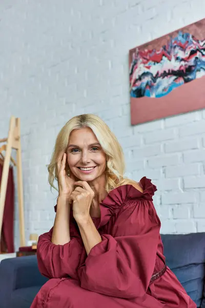 A mature sophisticated woman in a stylish dress sitting comfortably on top of a vibrant blue couch. — Stock Photo