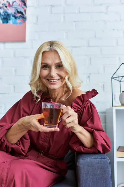 Stylish woman in chic dress relaxes on couch, savoring cup of tea. — Stock Photo