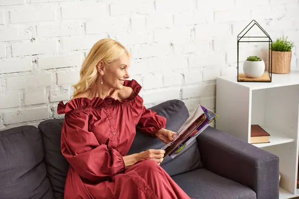 Donna sofisticata in abbigliamento elegante affascinato da una rivista su un divano accogliente. — Foto stock