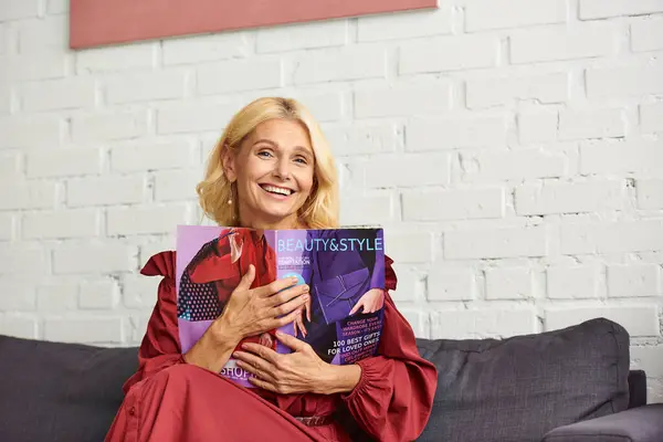 A sophisticated woman in stylish attire sits on a couch, engrossed in a captivating magazine. — Stock Photo