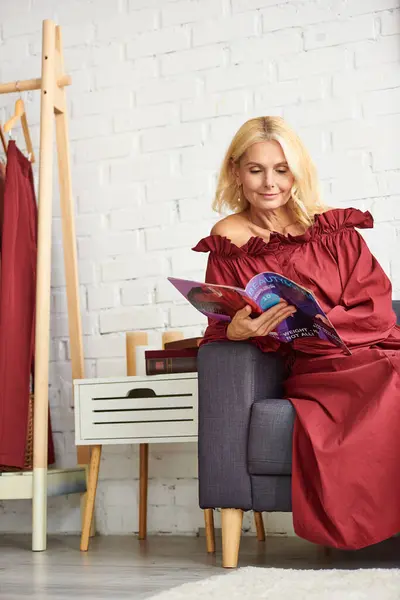 Reife Frau in stilvollem Kleid, versunken in der Lektüre einer Zeitschrift, während sie auf einem Stuhl sitzt. — Stockfoto