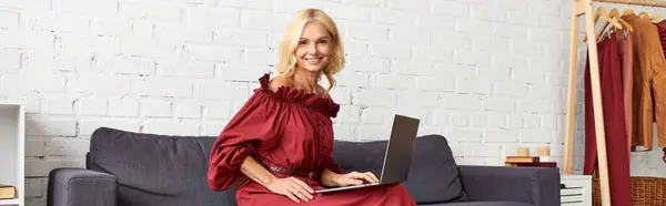 Mature woman in stylish dress using laptop on couch. — Stock Photo