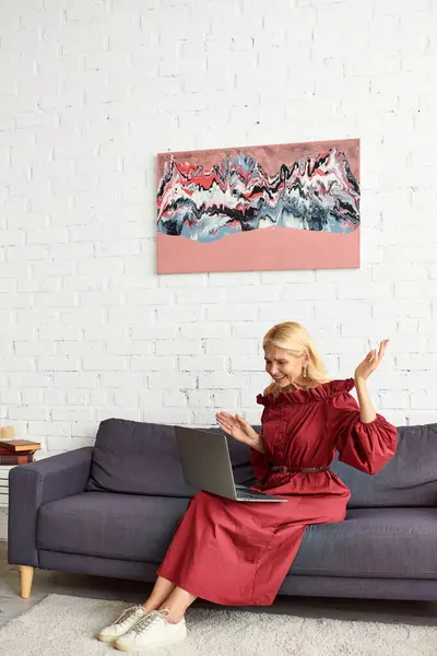 Stylish woman in a chic dress using a laptop on a comfortable couch. — Stock Photo