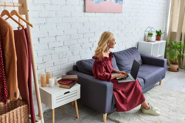 Гламурна жінка в шикарному вбранні, сидячи на дивані, захоплена своїм ноутбуком. — стокове фото