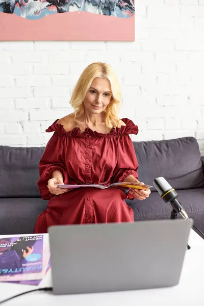 Donna matura in abito rosso registra podcast sulla bellezza femminile utilizzando il computer portatile. — Foto stock