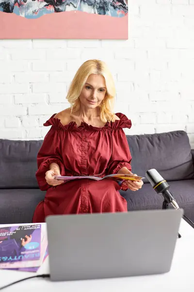 Donna matura in abito rosso registra podcast sulla bellezza femminile utilizzando il computer portatile. — Foto stock