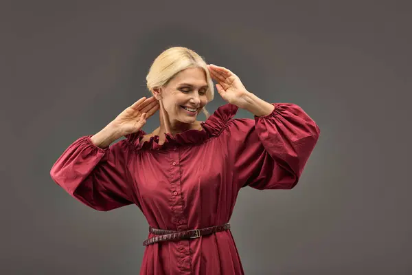 Mature woman in red dress posing with hands on her head. — Stock Photo