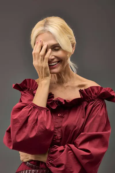 Mature woman in red top smiling and tenderly touching her face. — Stock Photo