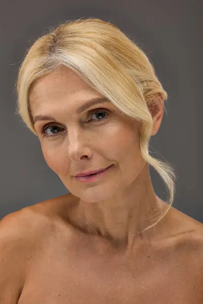 Pretty mature woman with blonde hair posing on gray backdrop. — Stock Photo