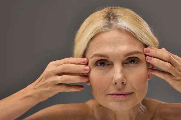 Mature woman gently touching her face with hands raised. — Stock Photo