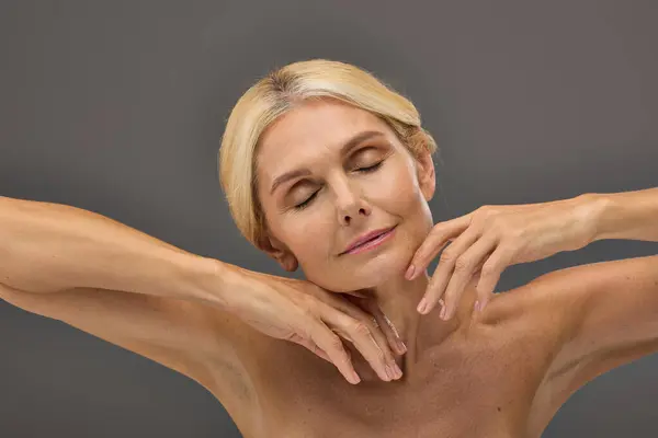 Appealing mature woman with blonde hair posing on gray backdrop. — Stock Photo