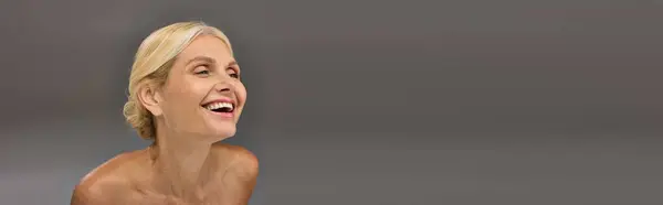 Uma mulher madura com um sorriso contra um pano de fundo cinza. — Fotografia de Stock