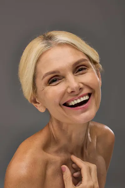 Eine reife Frau lächelt und posiert elegant vor grauem Hintergrund. — Stockfoto