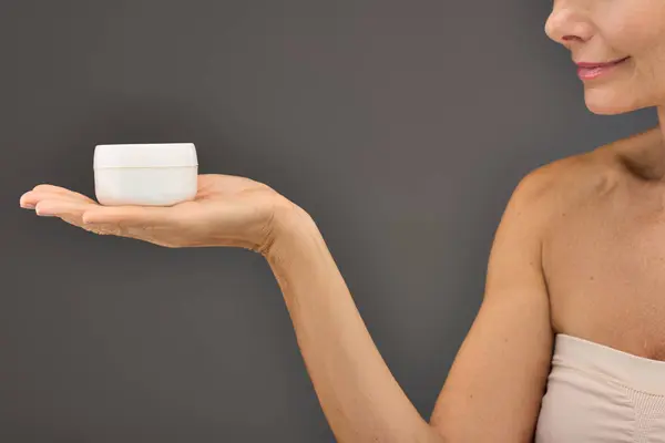 Donna matura elegantemente in possesso di una tazza di crema per la cura della pelle di routine. — Foto stock
