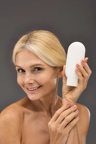 Beautiful mature woman holding locion on a gray backdrop. — Stock Photo
