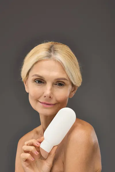 Appealing mature woman holding locion on a gray backdrop. — Stock Photo