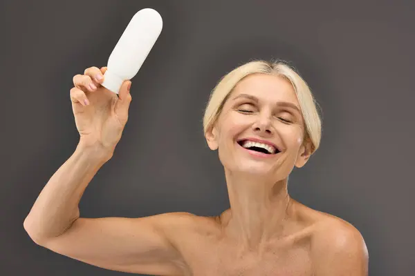 Charming mature woman holding locion on a gray backdrop. — Stock Photo