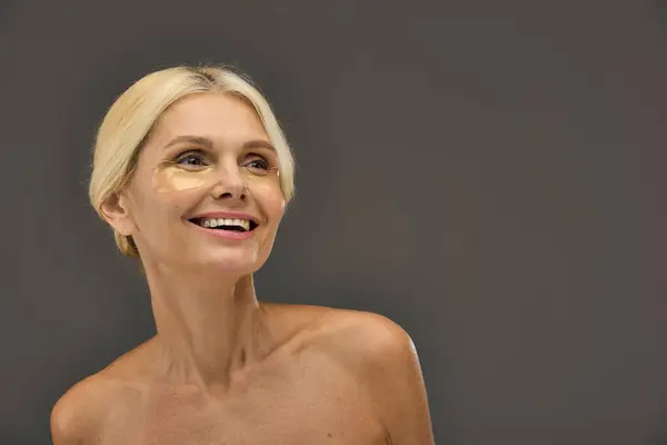 Appealing mature woman with blonde hair with eye patches on a gray backdrop. — Stock Photo