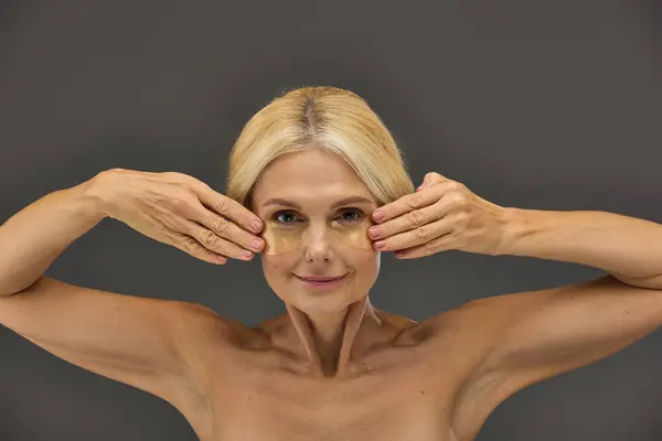 Charming mature woman with blonde hair with eye patches on a gray backdrop. — Stock Photo