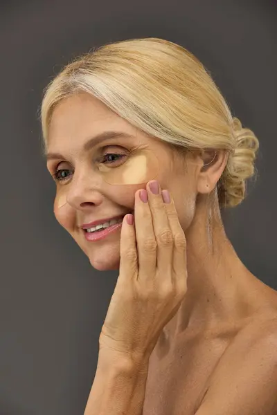 Blonde femme mature avec des patchs pour les yeux sur un fond gris. — Photo de stock
