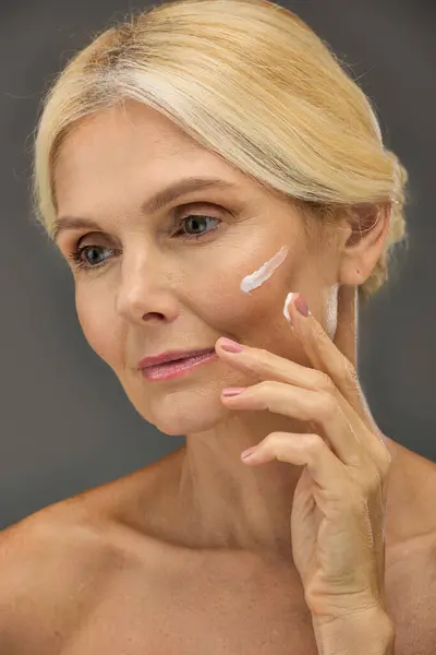 Mature woman with cream on face poses against a grey backdrop. — Stock Photo