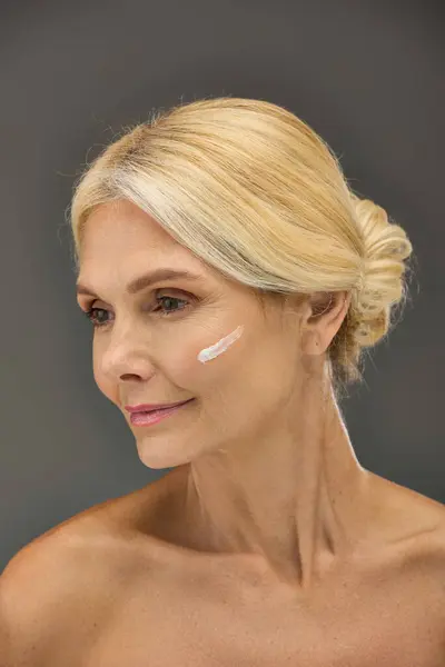 Mature woman showcasing her skincare routine with cream on face. — Stock Photo
