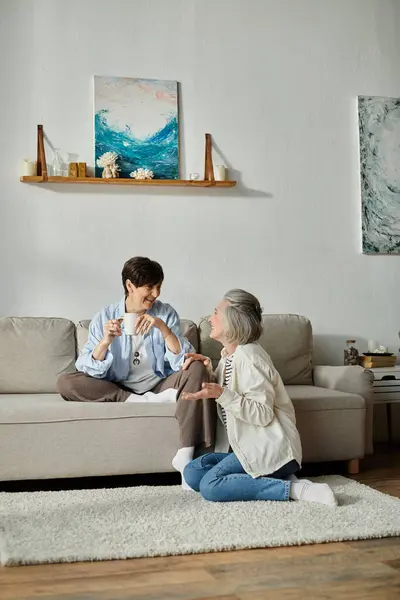 Two people, a loving mature lesbian couple, sitting on a couch in a living room. — Stock Photo