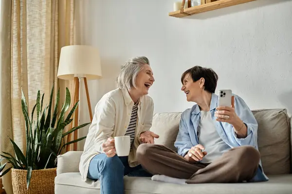 Loving lesbian couple laughing together on a cozy couch. — Stock Photo