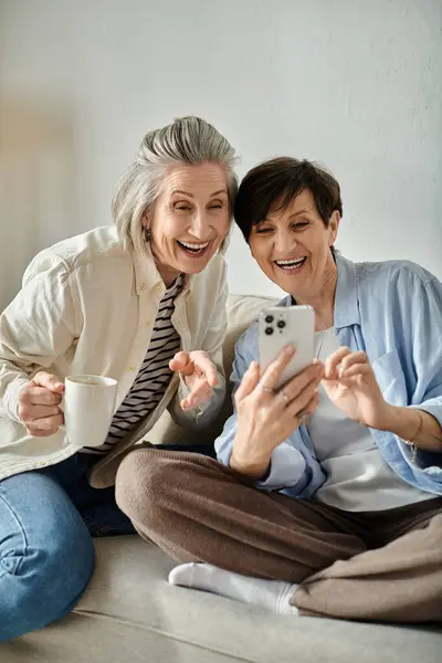 Zwei Frauen greifen auf einer gemütlichen Couch zu ihren Telefonen. — Stockfoto