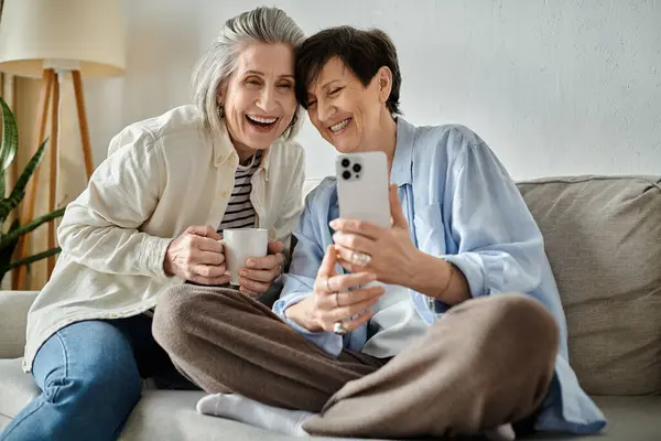 Two elderly women sitting on a couch, happily taking a selfie together. — Stock Photo