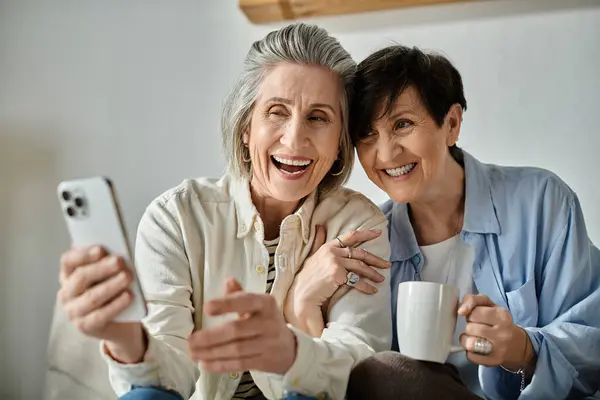 Two elderly women sit on a couch, enjoying a cup of coffee together. — Stock Photo