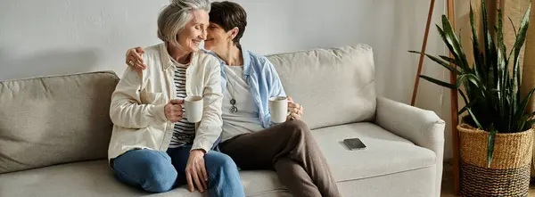 Dos personas mayores, una pareja lesbiana madura amorosa, se sientan de cerca en un sofá. - foto de stock